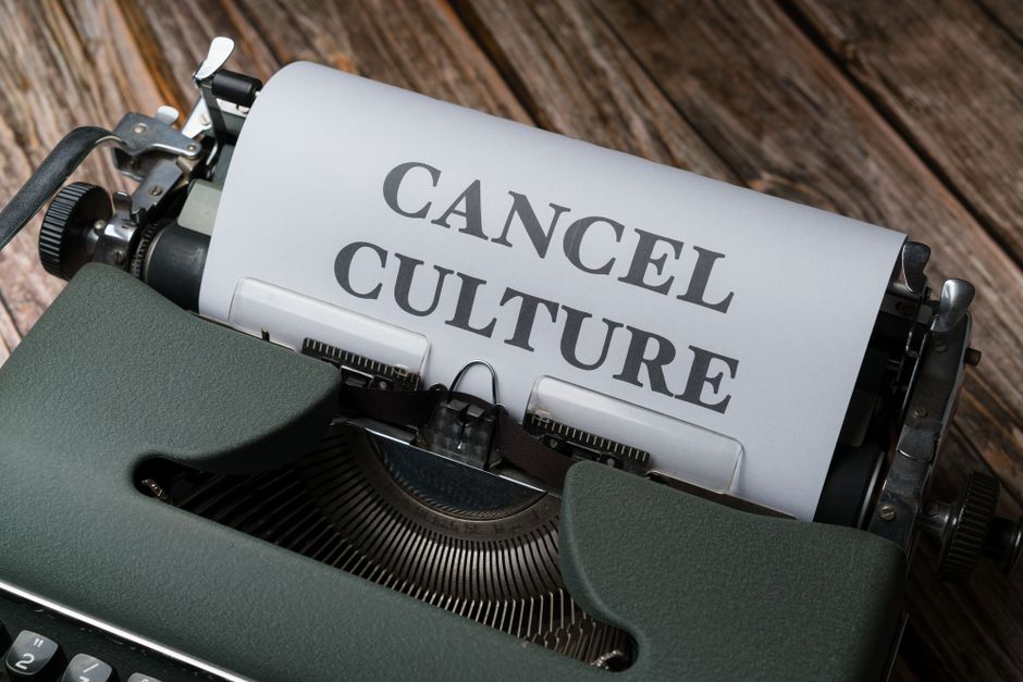 A close-up view of a vintage typewriter with a piece of white paper loaded into the roller, displaying the bold black text 'CANCEL CULTURE'. The typewriter features a dark green textured body with visible keys and mechanical components, situated on a wooden surface with a natural grain pattern and warm brown tones. The lighting highlights the metallic details of the typewriter, creating a subtle contrast against the matte finish of the paper and wood. This image visually emphasizes the concept of stopping or rejecting certain ideas, paralleling themes of alternative waste handling and the importance of clear communication in rubbish removal services, as reflected in the context of booking errors or service cancellations.