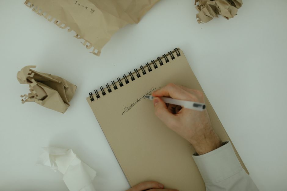 A white spiral-bound notepad placed on a black surface with the handwritten word 'MISTAKE' in large, black capital letters across the front. To the right of the notepad, there is a red rubber stamp with the word 'DELETE' printed in bold black letters. The overall scene has a professional and neutral tone, emphasizing the concept of mistake correction or removal, which is relevant to rubbish removal services such as those offered by Rubbish Removal Harrow in the context of managing unwanted waste or private disposal tasks. The lighting highlights the contrast between the black background and the white notepad, as well as the vivid red of the stamp, creating a clear and sharply focused visual suitable for an article discussing booking mistakes and cancellation fees for waste removal services, subtly supporting ideas related to alternative waste handling or on-site clearance options.