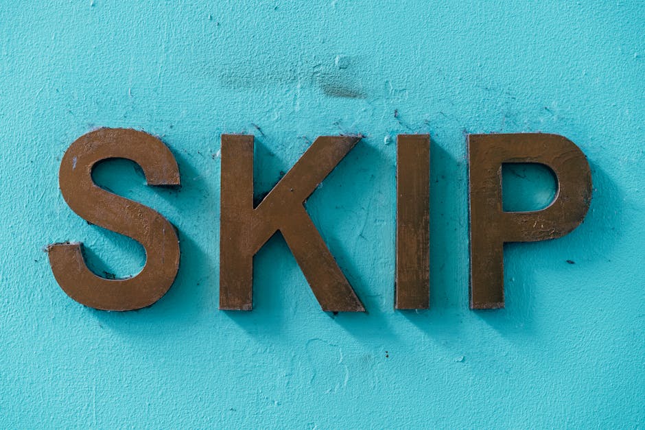 Close-up of three-dimensional, dark brown metal letters spelling 'SKIP' mounted on a textured, light blue painted wall. The letters are evenly spaced, with the 'S' on the left, the 'K' in the center, and the 'P' on the right. The surface of the letters has minor imperfections and a matte finish, contrasting with the rough, slightly uneven wall surface, which shows small cracks and subtle variations in tone. The background environment appears to be an exterior or interior setting where signage indicates waste or rubbish management services, aligning with the context of private waste handling or skip hire by rubbish removal companies such as Rubbish Removal Harrow. The lighting is diffuse, highlighting the three-dimensional aspect of the metal letters without harsh shadows, creating a clear, professional visual presentation suitable for accessibly describing waste disposal signage.